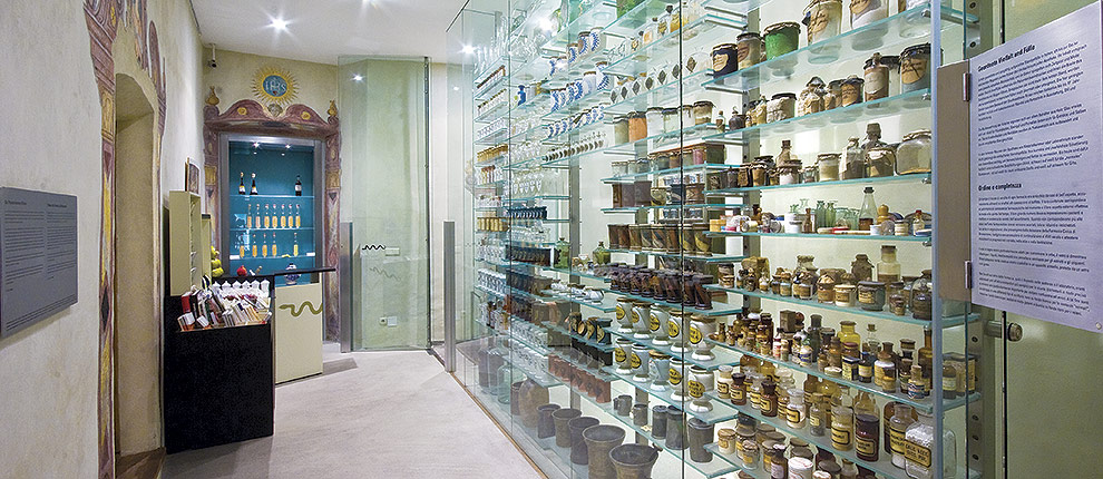 Schauregal aus Glas mit alten Apothekengefäßen, Türrahmen mit Seccomalerei im Eingangsbereich des Pharmaziemuseum Brixen.